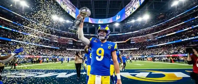 Matthew Stafford in a blue and yellow Los Angeles Rams uniform #9 holding the Lombardi Trophy aloft under golden confetti at SoFi Stadium.